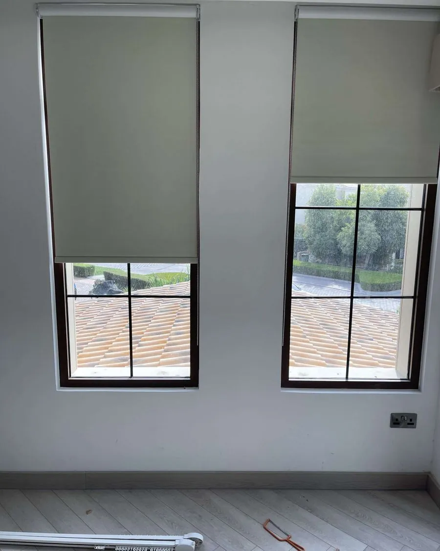 Sage green premium roller blinds on two windows in a UAE home